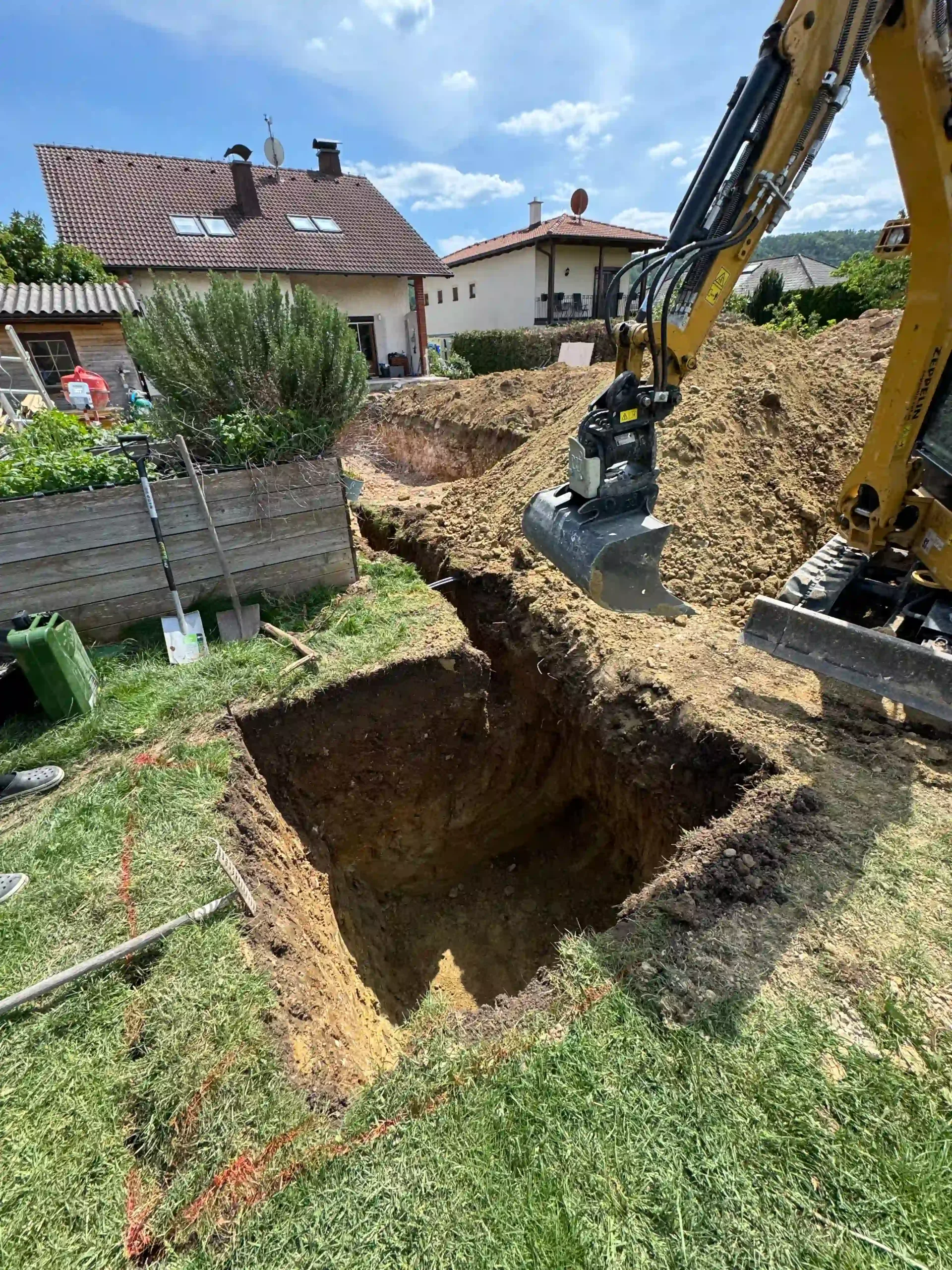 Baugrube im Garten, am Rand steht ein Bagger